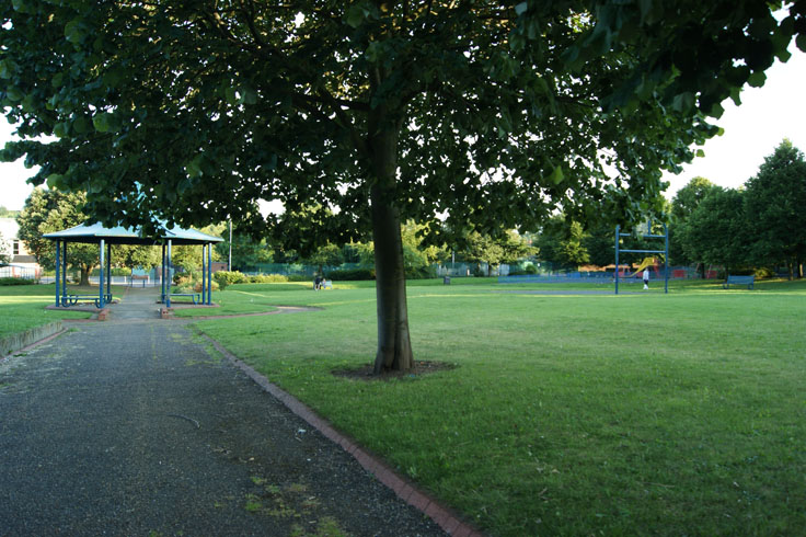 A bandstand, trees and a basketball hoop. 